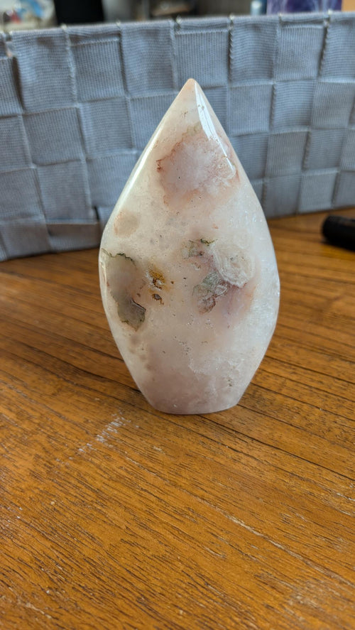 Gepolijste punt van Bloemagaat met zachte roze en witte patronen op een houten ondergrond, 10 cm hoog en 245 gram.