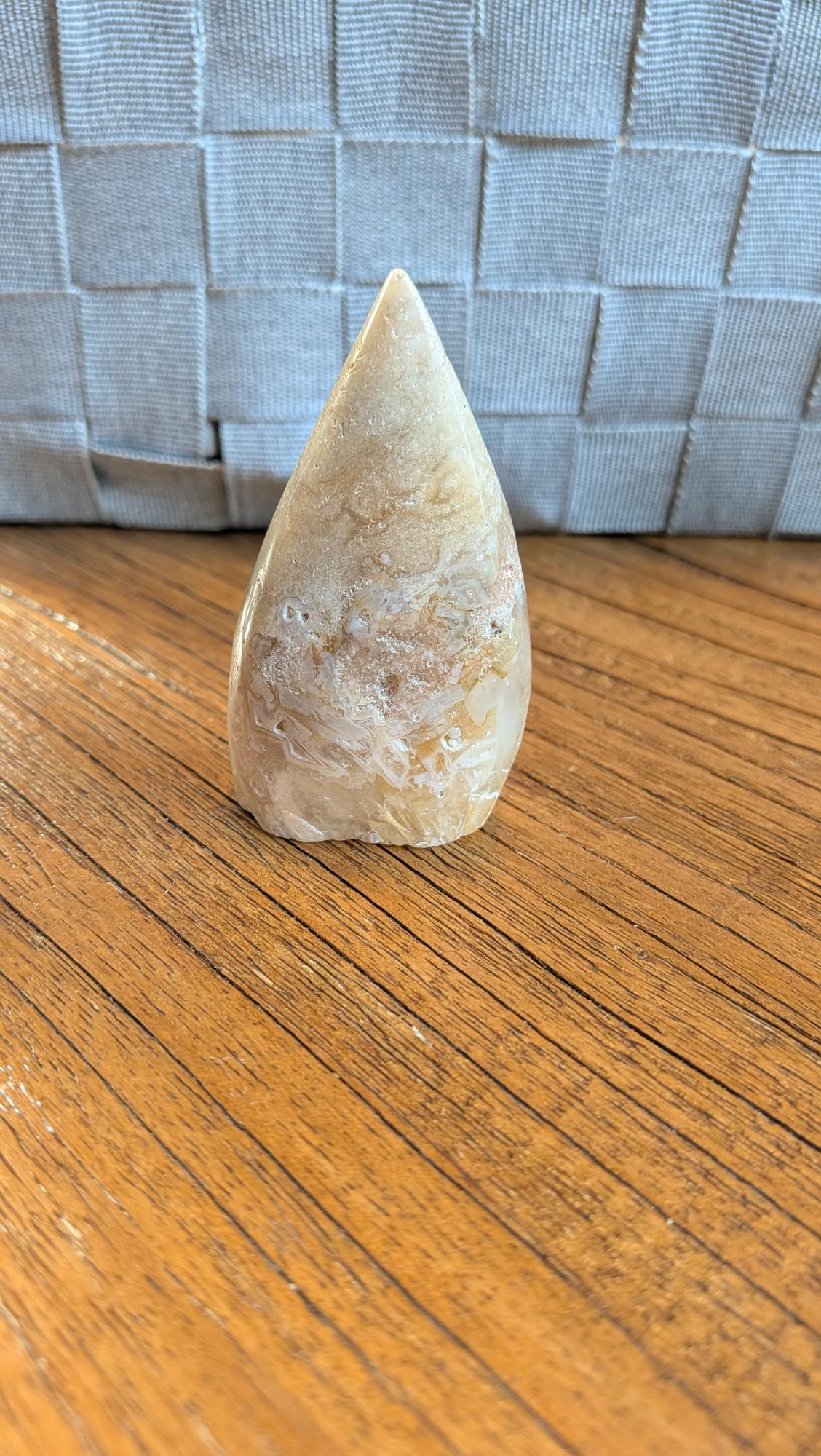 Handgepolijste Bloemagaat vrije vorm van 8 cm hoog met zachte roze tinten en witte bloempatronen op een houten ondergrond.