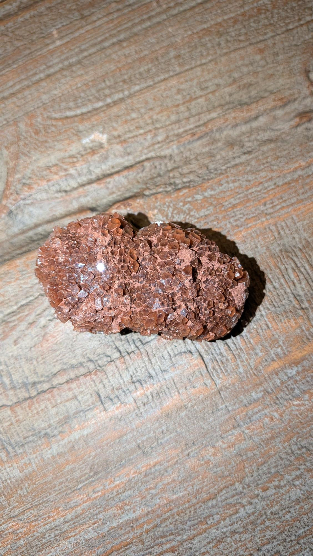Close-up van een roodbruine Aragoniet Sputnik cluster van 64 gram met zeshoekige kristalstructuur op een houten achtergrond.