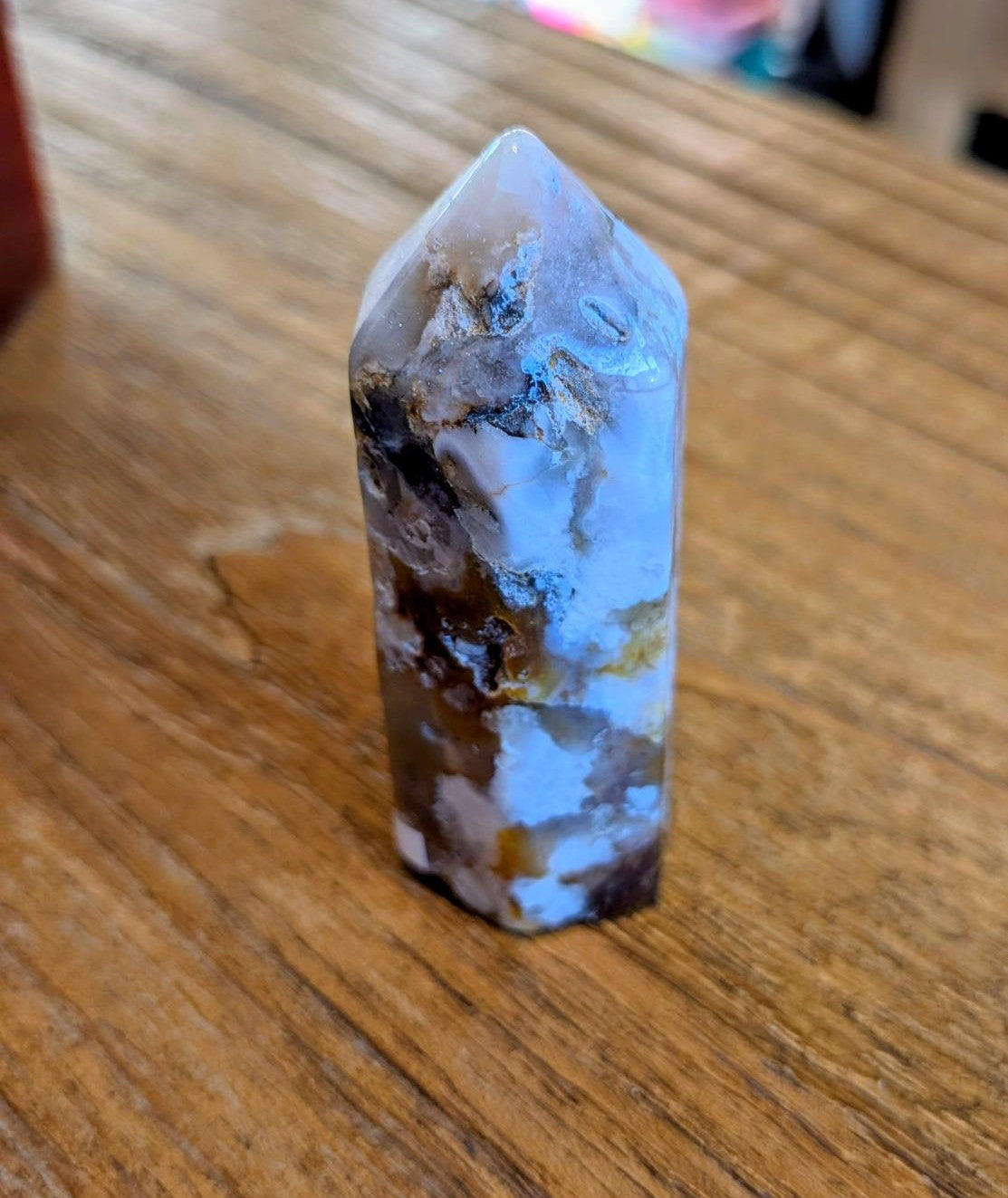 Stevige Bloem Agaat kristal toren van 7 cm hoog met witte bloemtekeningen en 70 gram gewicht op een houten achtergrond.