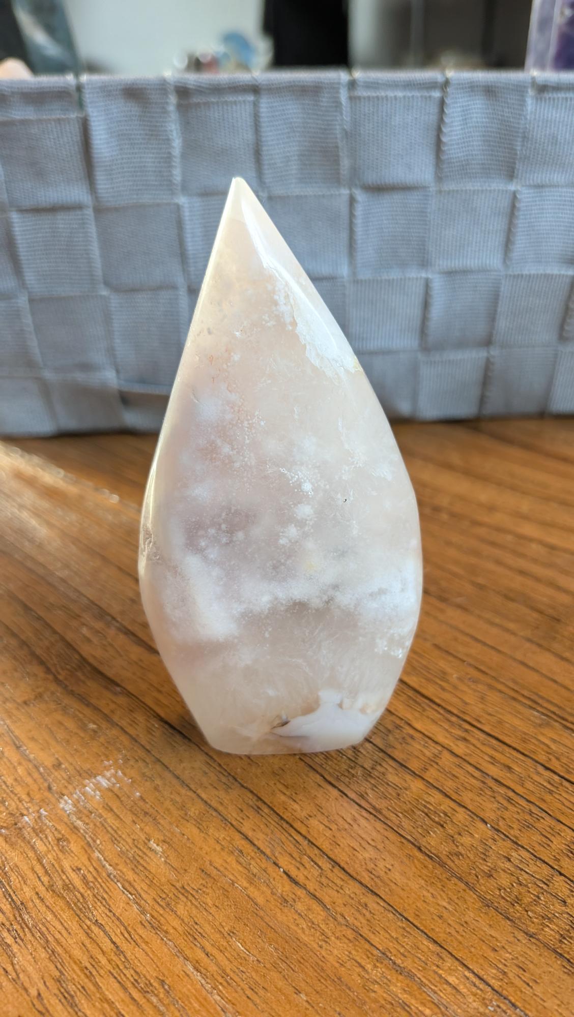 Handgepolijste Bloemagaat vrije vorm van 10 cm hoog met zachte roze tinten en witte bloempatronen op een houten tafel.