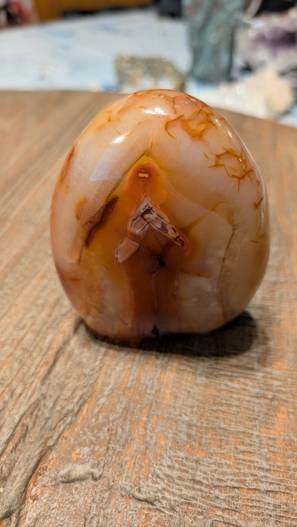 Gepolijste oranje Carneool freeform van 264 gram met natuurlijke bandenstructuur op een houten ondergrond.