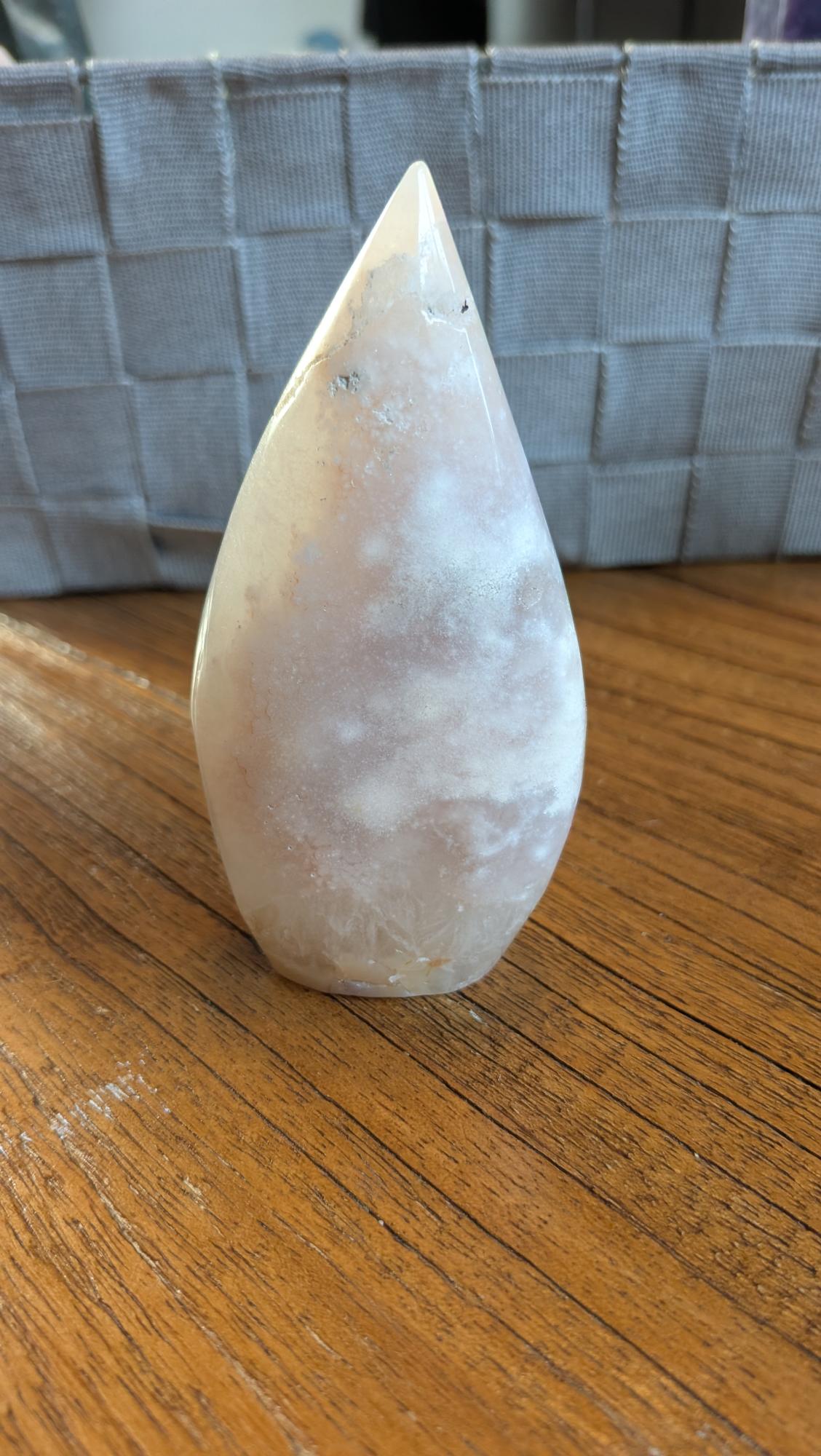 Handgepolijste Bloemagaat vrije vorm van 10 cm hoog met zachte roze tinten en witte bloempatronen op een houten tafel.