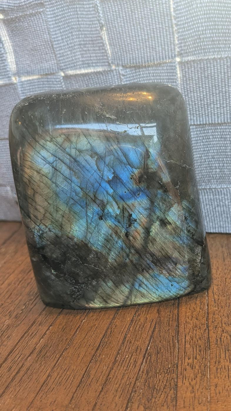 "Handgepolijste vrije vorm van Labradoriet met een intense blauwe en gouden glans, 9 cm hoog en 473 gram, getoond in een hand om de schittering te laten zien."