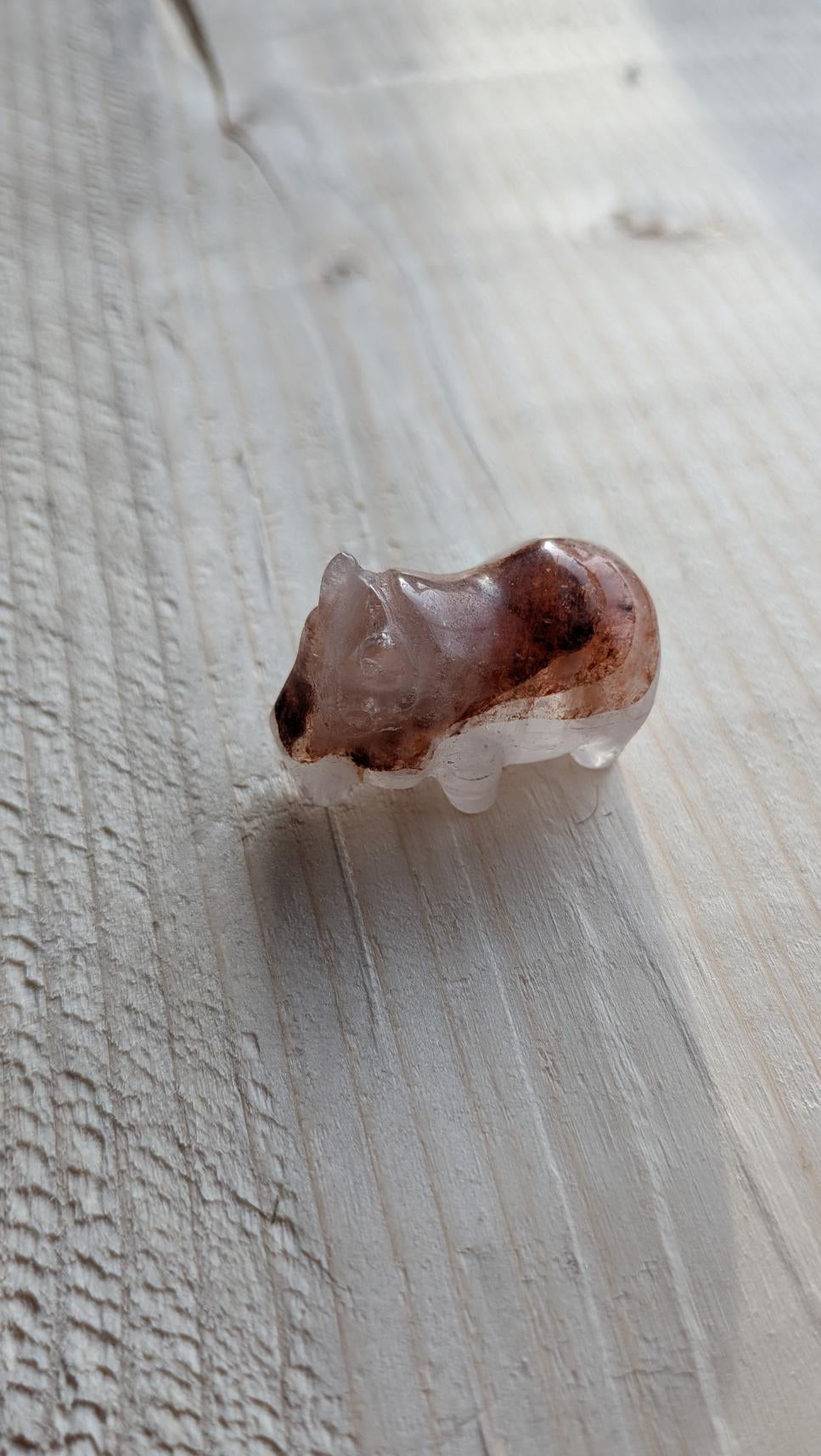 Handgesneden mini nijlpaardje van lithium kwarts (3 cm) op een lichte houten ondergrond.