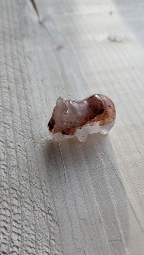 Handgesneden mini nijlpaardje van lithium kwarts (3 cm) op een lichte houten ondergrond.