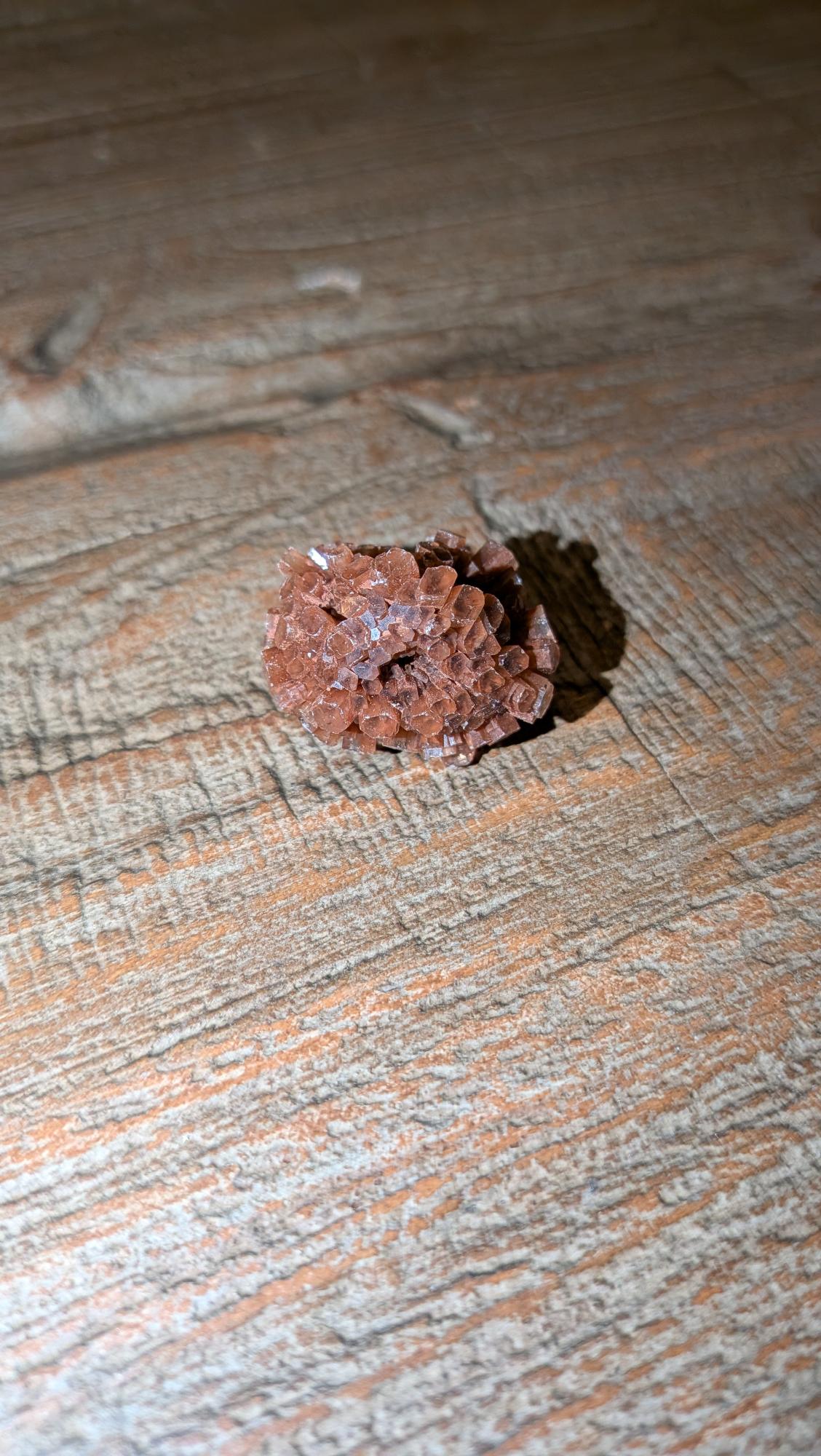 Klein, symmetrisch roodbruin Aragoniet Sputnik kristal van 12 gram op een houten ondergrond.