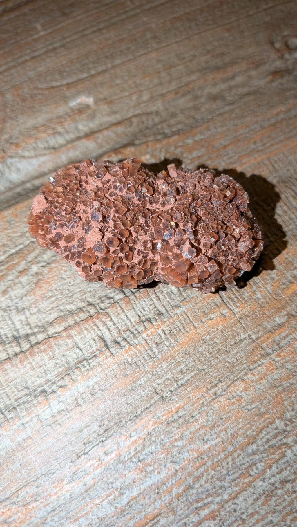 Close-up van een roodbruine Aragoniet Sputnik cluster van 64 gram met zeshoekige kristalstructuur op een houten achtergrond.