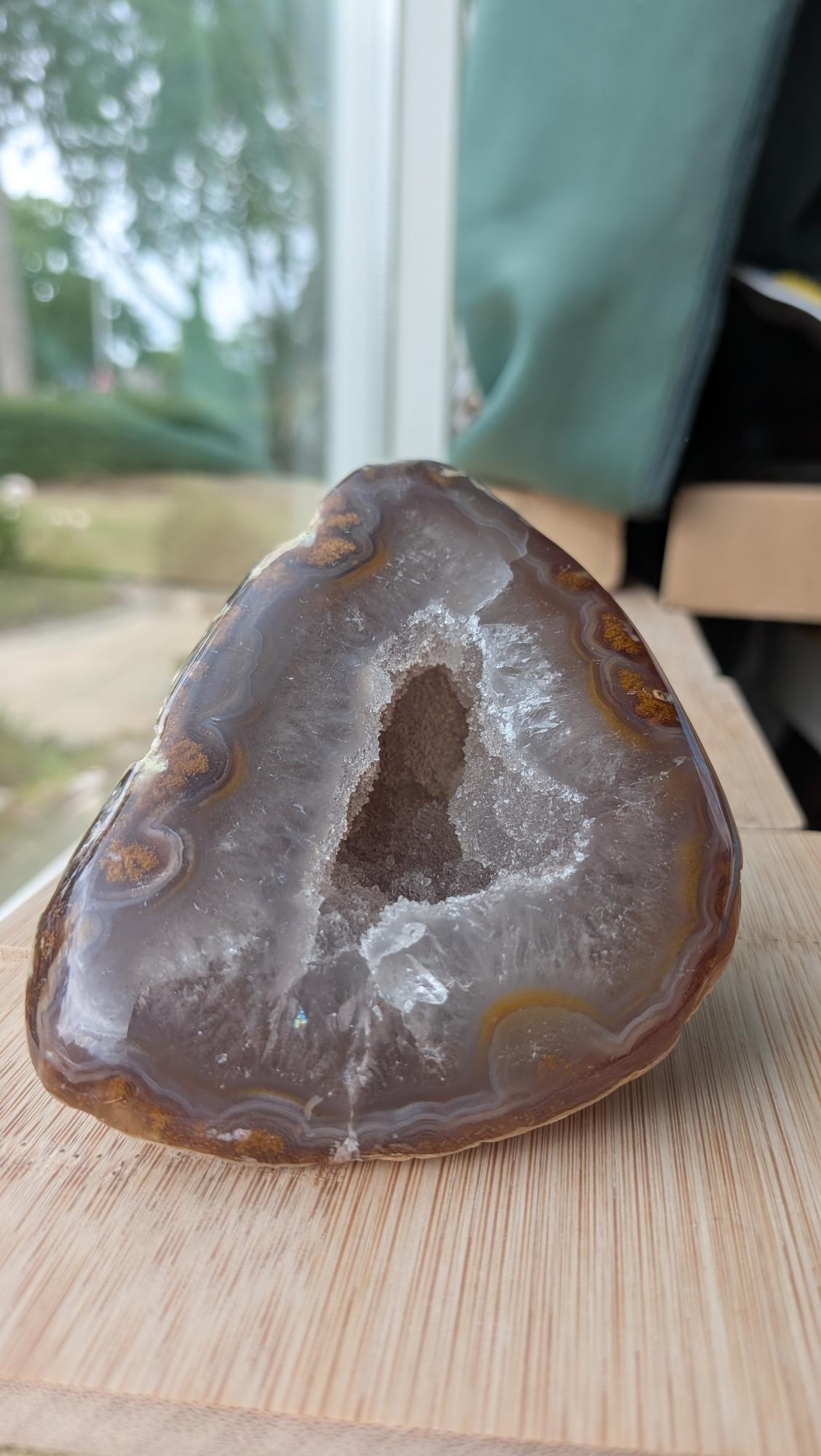 Een hand houdt een Agaat-geode van 500 gram vast met gelaagde aardetinten en een sprankelend kristalhart in het midden