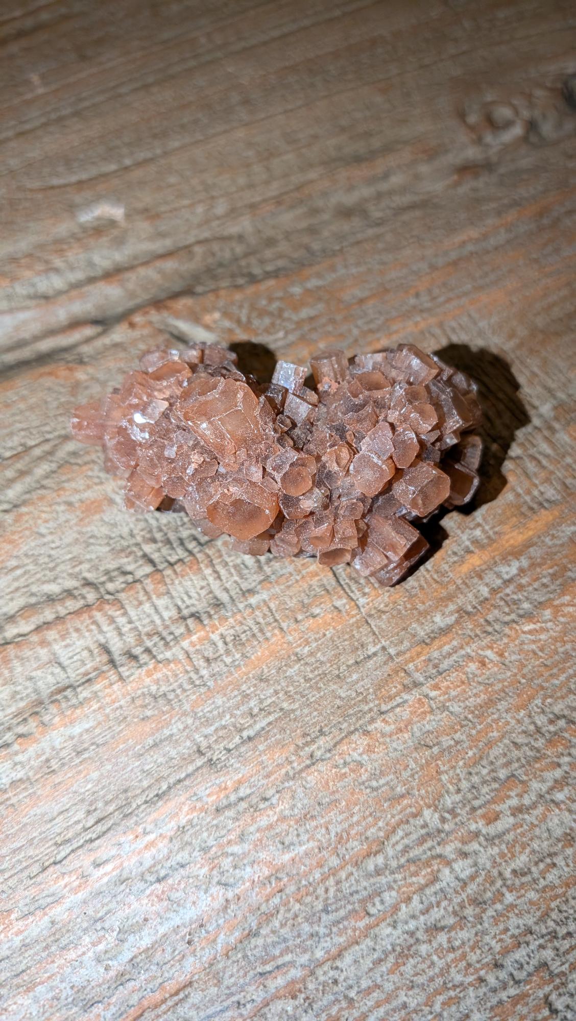 Langgerekt roodbruin Aragoniet cluster van 54 gram met duidelijke kristalprisma's op een houten achtergrond.