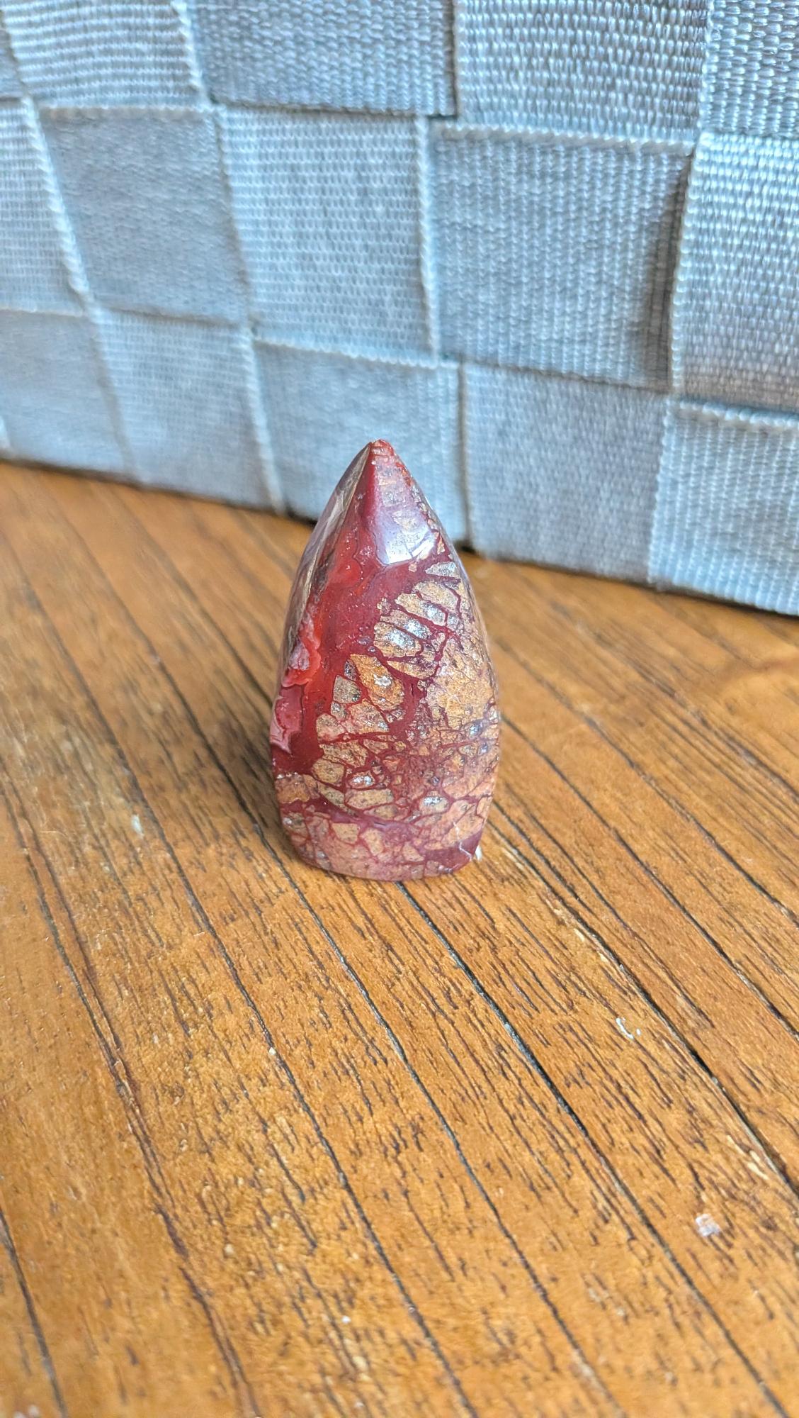 "Kleine gepolijste Crazy Lace Agaat vrije vorm met dieprode en bruine patronen, 4 cm hoog en 21 gram, staand op een houten ondergrond."