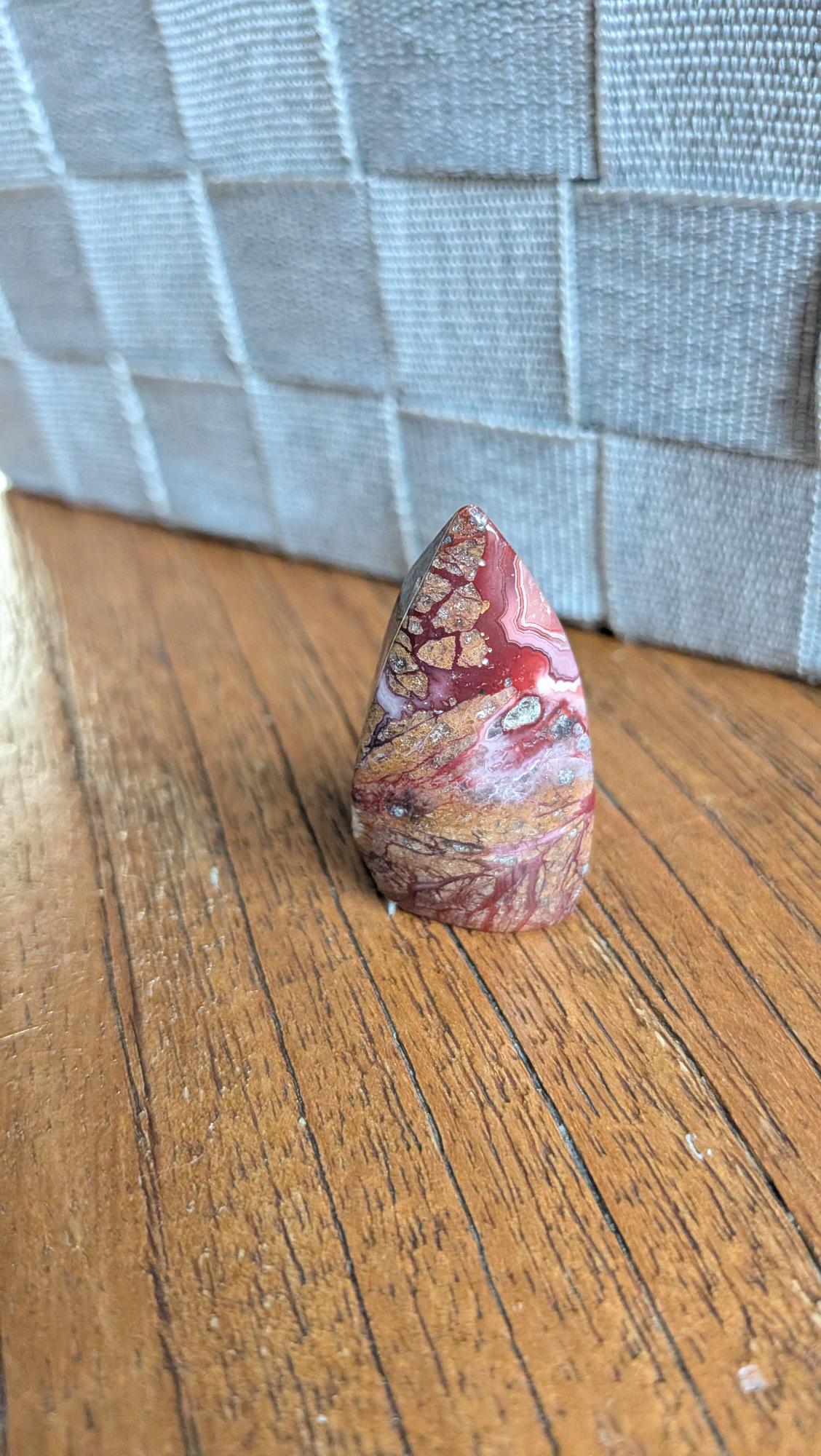 "Kleine gepolijste Crazy Lace Agaat vrije vorm met dieprode en bruine patronen, 4 cm hoog en 21 gram, staand op een houten ondergrond."