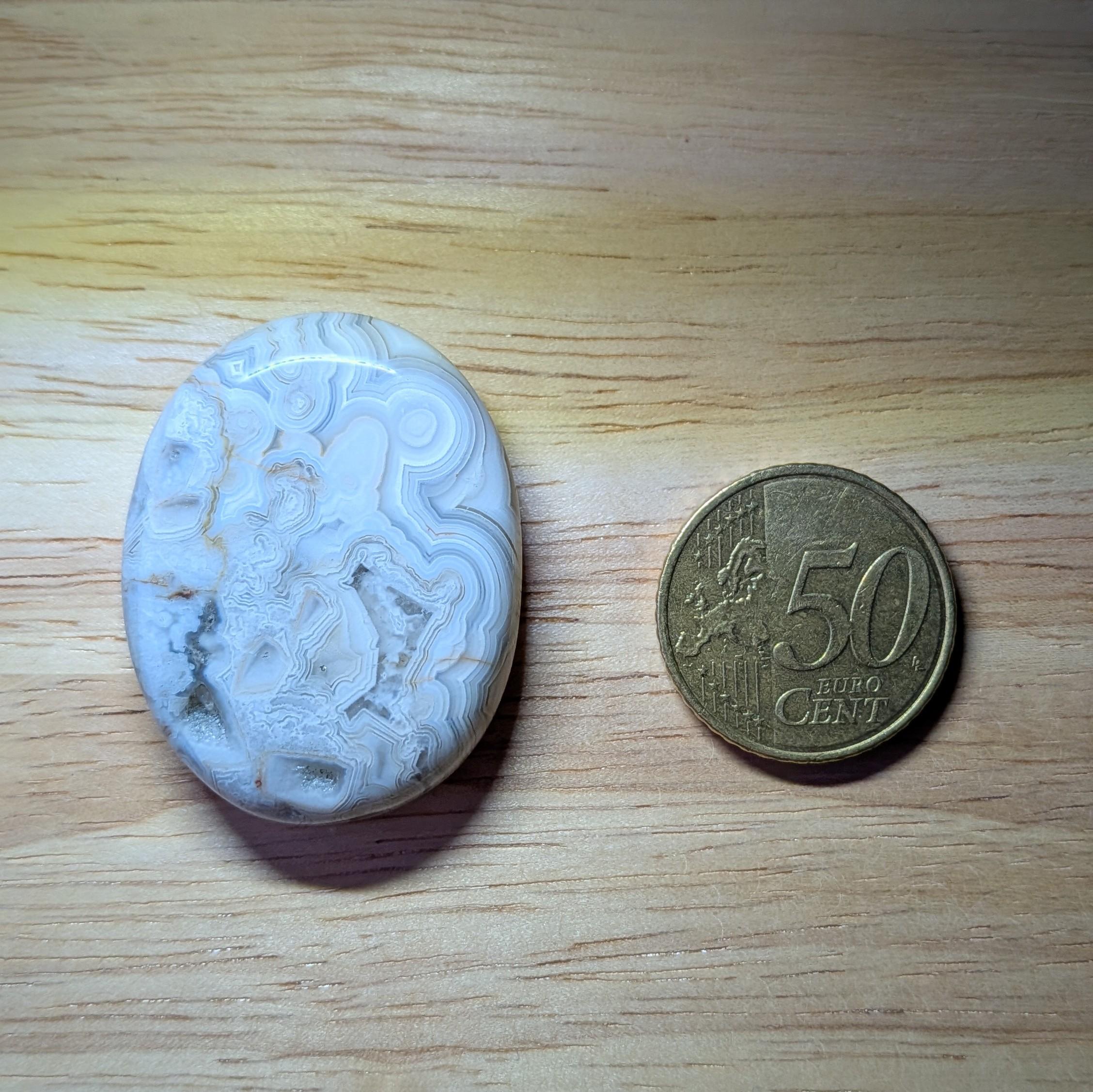 Ovaal geslepen Crazy Lace Agaat met een complex wit en grijs lijnenpatroon naast een 50 eurocent munt.