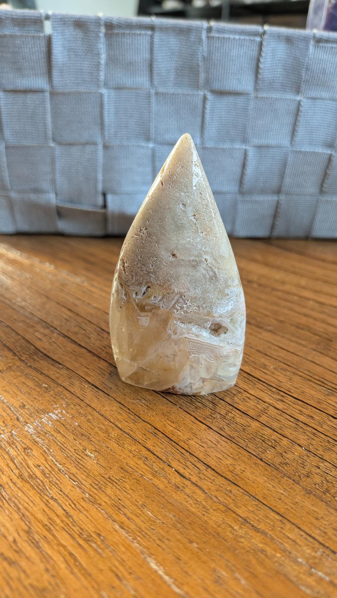 Handgepolijste Bloemagaat vrije vorm van 8 cm hoog met zachte roze tinten en witte bloempatronen op een houten ondergrond.