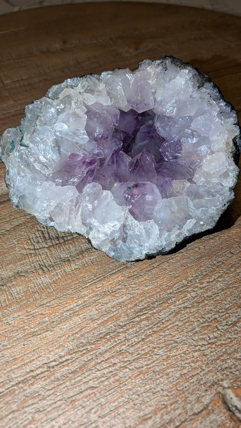 Paars Amethist kristal cluster in een donkere geode van 819 gram op een houten ondergrond.