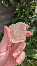 Een hand houdt een sprankelende suiker druzy chalcedoon van 44 gram vast, met een fijne, suikerachtige kristaltextuur